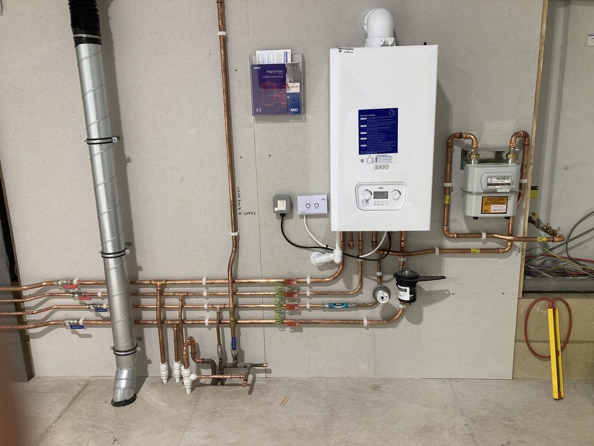 A Baxi boiler installed by D W Plumbing and Heating, with the copper pipework, gas meter and flue neatly run and labelled