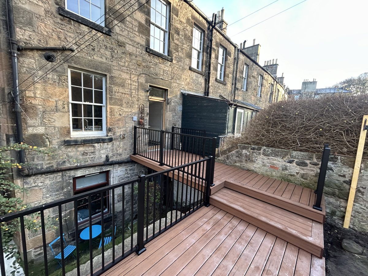 A split level composite deck with black metal balustrade built by Mitchell Landscaping behind a traditional stone terraced house