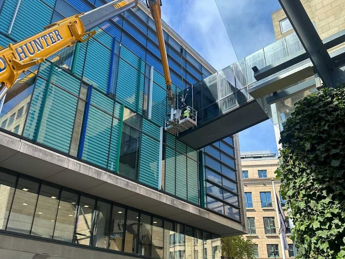 A crane lifting a glazing unit to an upper floor of a modern commercial building in central Edinburgh, with an operative working from a suspended platform