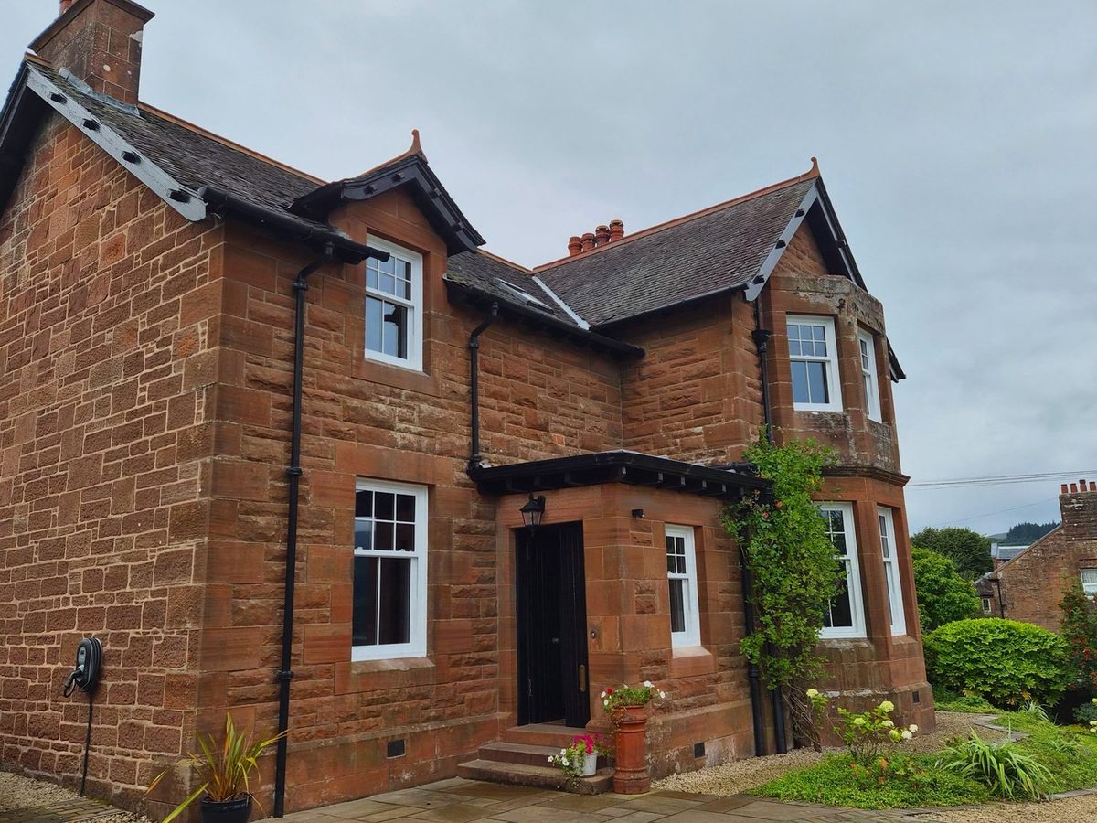 A red sandstone villa on Arran with newly installed white vertical sliding sash windows, including a bay and a dormer