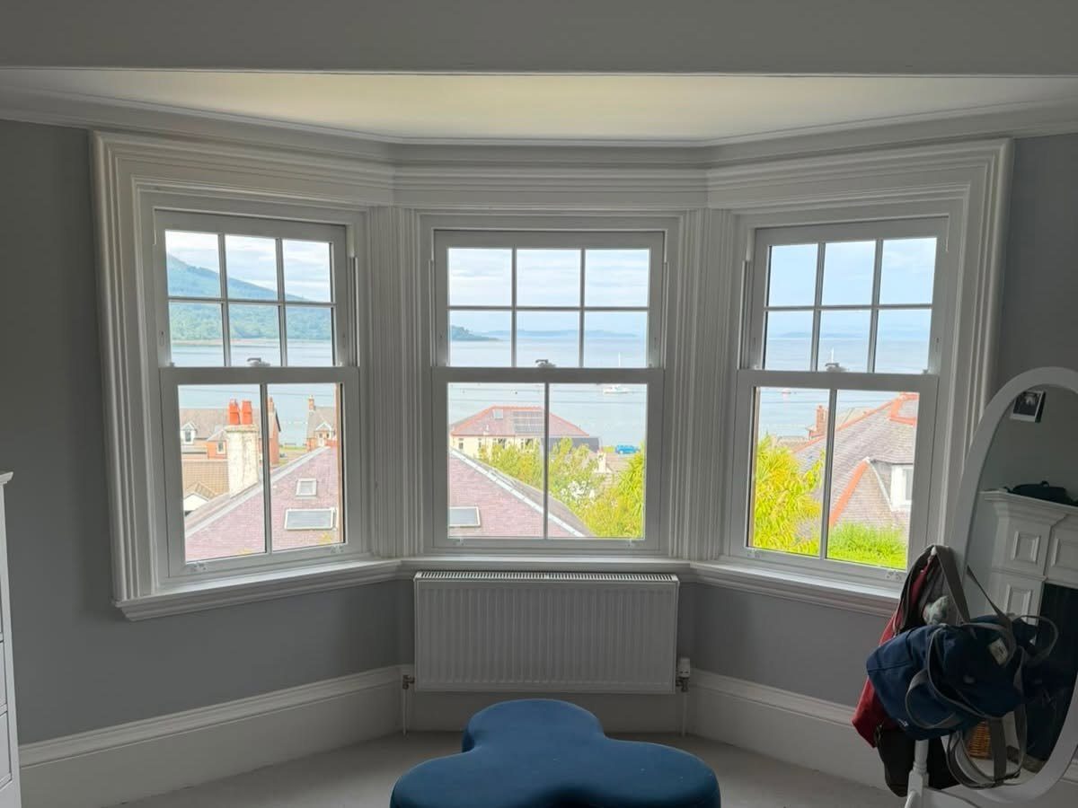 The inside of a bay window fitted by RMC Double Glazing, with three vertical sliding sashes looking out over rooftops to the Firth of Clyde
