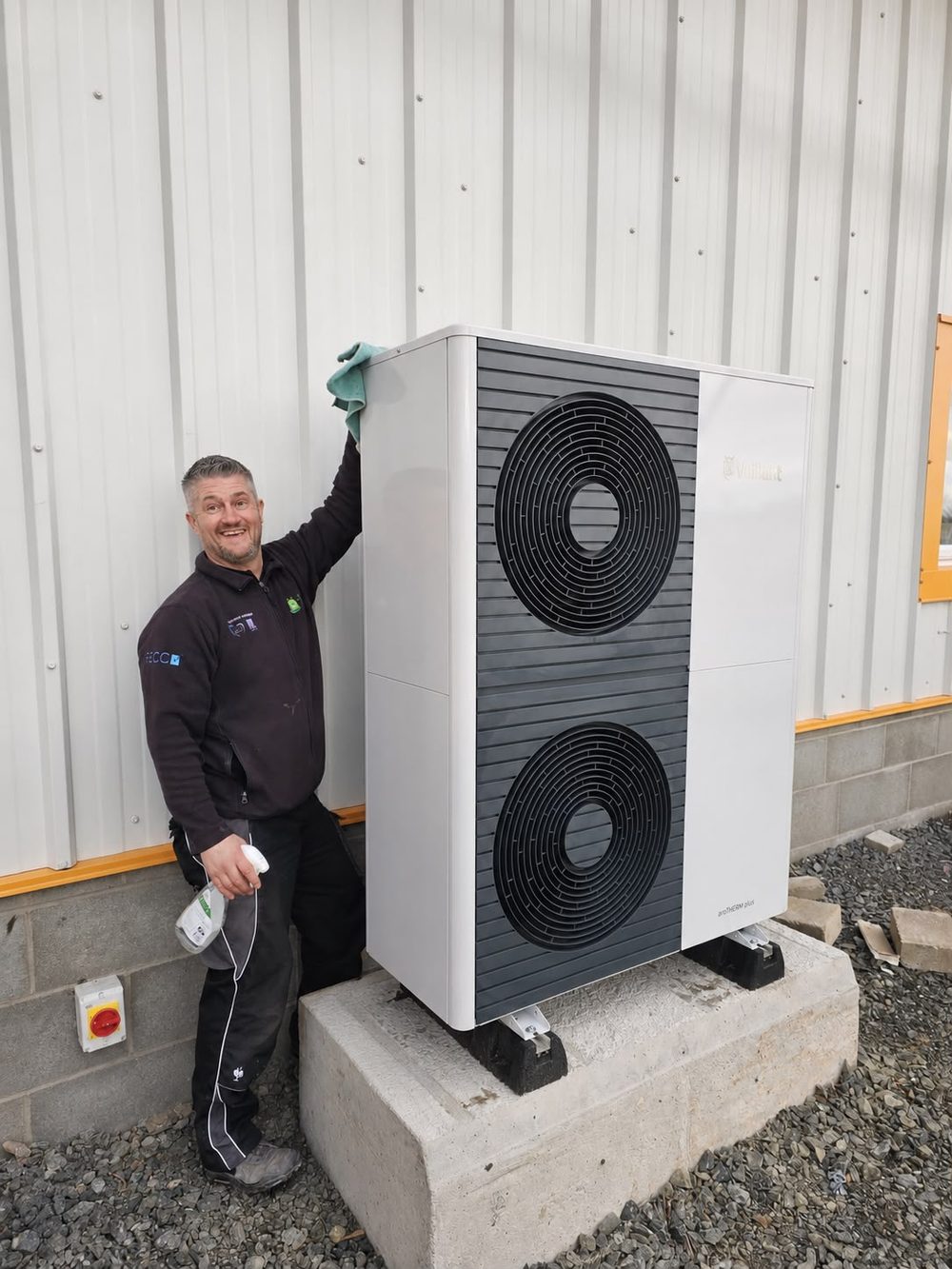An S and P Renewables engineer beside a newly commissioned air source heat pump mounted on a plinth outside a house in the Scottish Borders